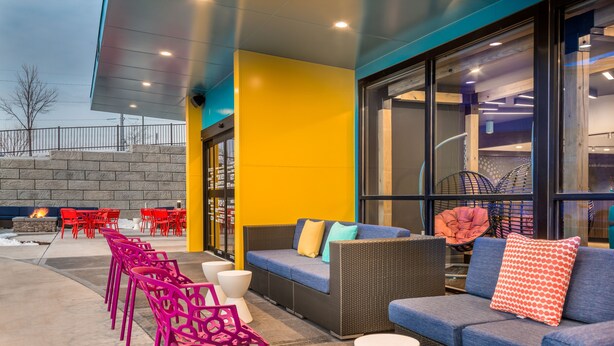 An outdoor seating area with wicker sofas and chairs, a fire feature, and a stone wall. - Tru by Hilton Madison West, WI (Madison)