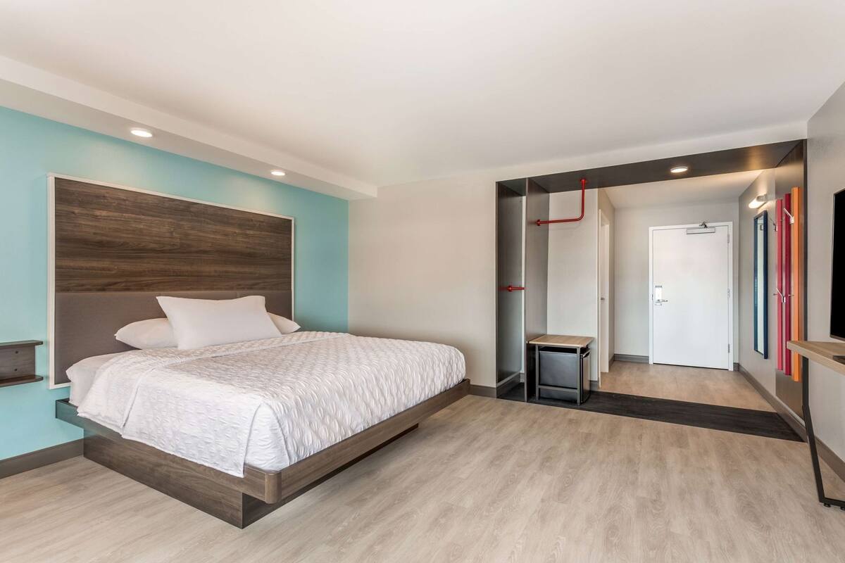 Une chambre à coucher avec un lit, une table de chevet, un petit tabouret, une porte et un miroir.