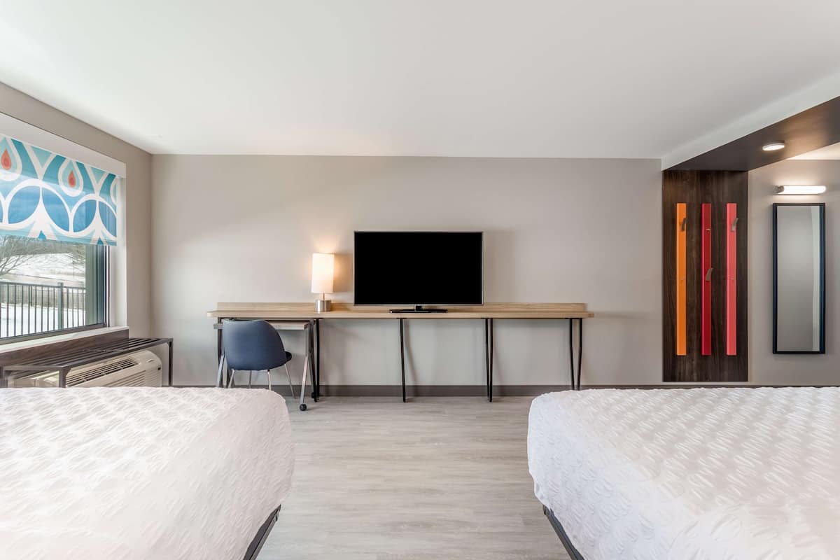 Une chambre d’hôtel avec deux lits, un bureau avec une télévision, une chaise et une fenêtre donnant sur un beau paysage.