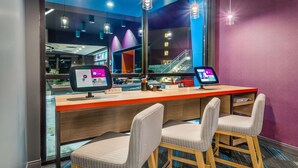 A reception desk with two computer monitors, a wooden counter, and two upholstered chairs. - Tru by Hilton Madison West, WI (Madison)