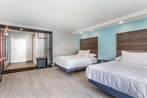 A hotel room with two beds, a small desk, a chair, a trash bin, and a door leading to another room. - Tru by Hilton Madison West, WI (Madison)