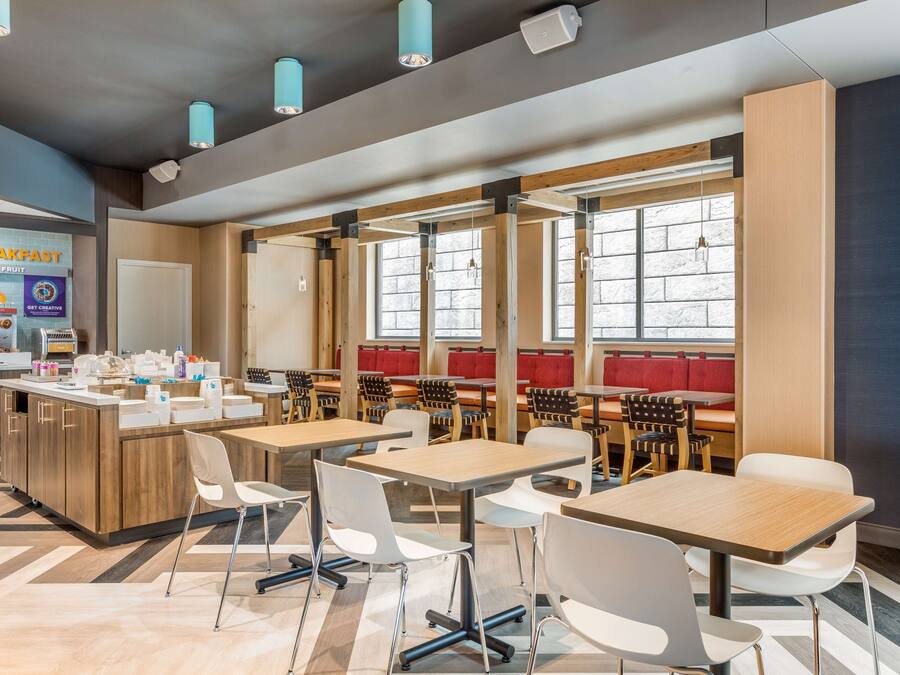 A modern dining area with wooden tables and chairs, a breakfast counter, and large windows providing natural light.