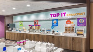 A breakfast area with a sign reading "TOP IT BREAKFAST" and sections for coffee, donuts, yogurt, oatmeal, and fruit. - Tru by Hilton Madison West, WI (Madison)