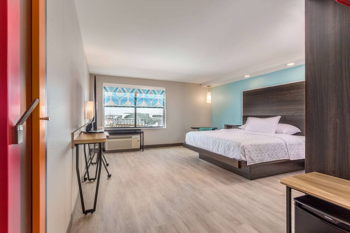 Une chambre d’hôtel moderne équipée d’un lit, d’un bureau et d’une fenêtre donnant sur la ville.