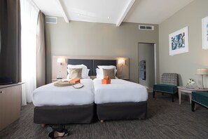 Habitación de hotel con dos camas, un escritorio, una silla y una mesita de noche con lámpara.
