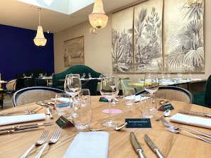 Une salle de restaurant avec des tables dressées pour le service, où l’on peut admirer de la belle verrerie et des couverts élégants.