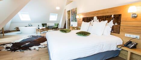 A spacious bedroom with a large bed, wooden headboard, and a wooden floor. There is a small bedside table with a lamp and a phone.