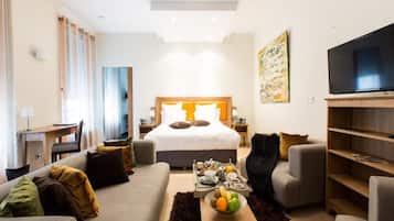 Ein modernes Hotelzimmer mit einem großen Bett, einem Fernseher, einem Essbereich und einer gemütlichen Sitzecke.