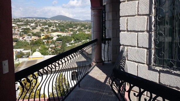 A balcony with a wrought iron railing, a stone wall, and a window with decorative iron bars. - Posada Y Bungalows La Capilla (Ezequiel Montes)