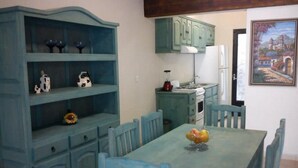 A dining area with a blue table and matching chairs, a blue cabinet with shelves, and a painting on the wall. - Posada Y Bungalows La Capilla (Ezequiel Montes)
