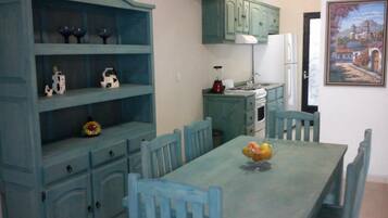 A dining area with a blue table and matching chairs, a blue cabinet with shelves, and a painting on the wall.