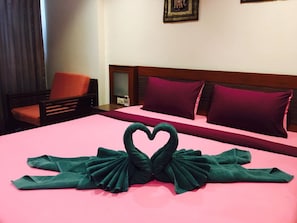 A hotel room with a bed, a chair, and a heart-shaped towel decoration.