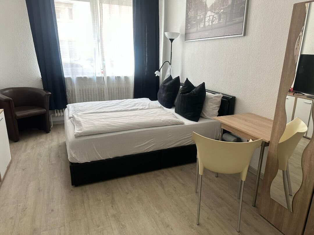 A hotel room with a bed, a desk, a chair, a lamp, and a window with curtains.