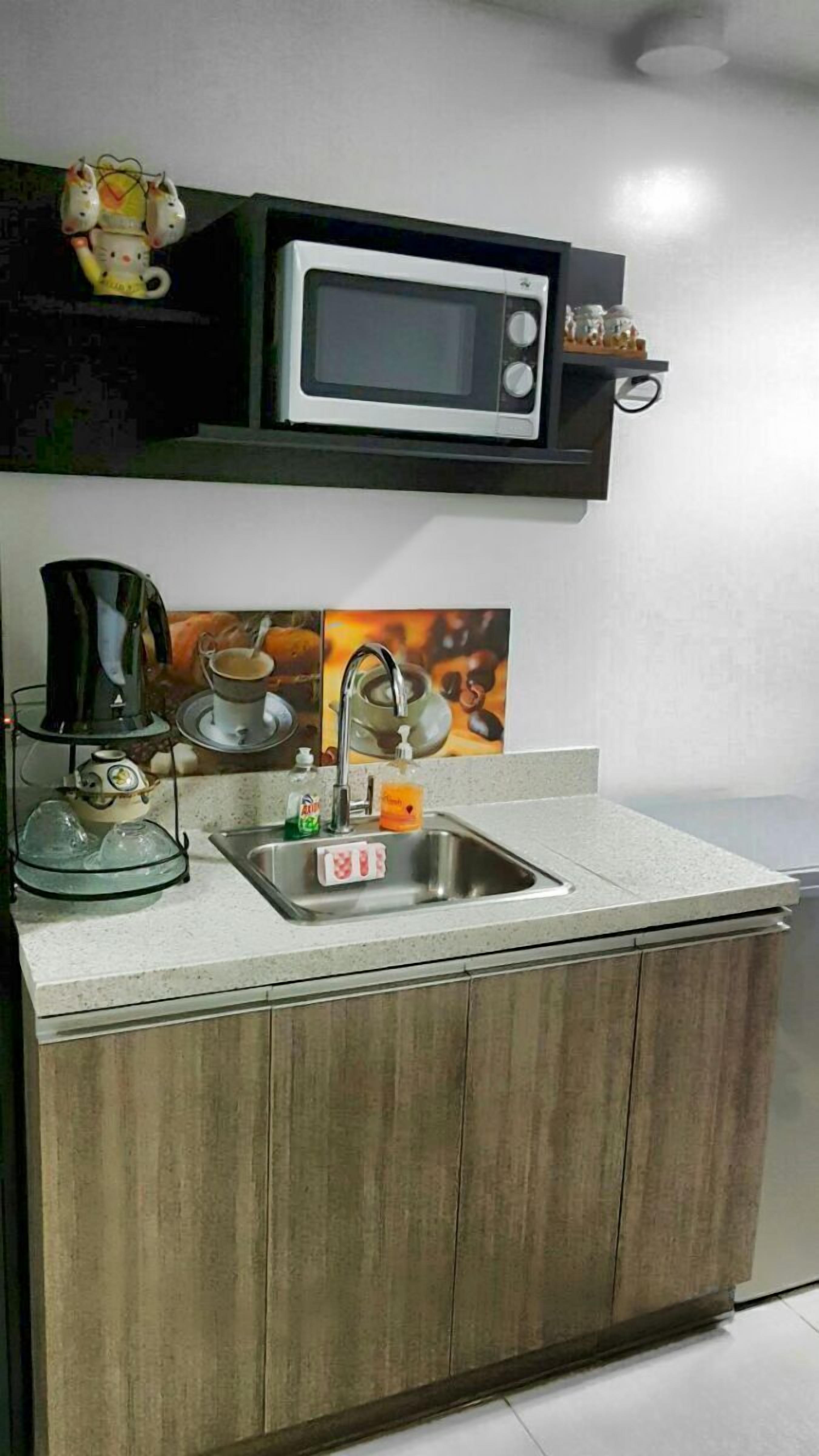 Una cocina compacta con microondas, lavamanos y armarios de madera.