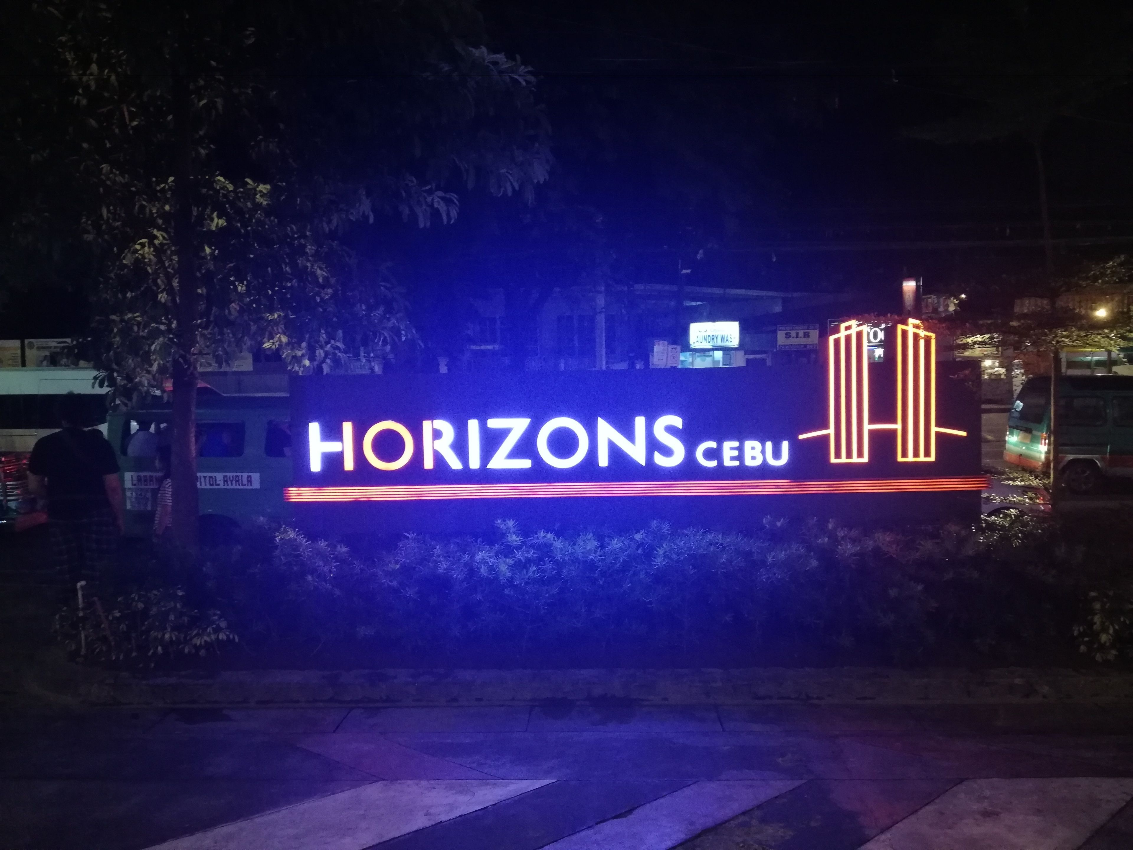 Une enseigne nocturne pour l’hôtel Horizons Cebu, avec un texte illuminé et un symbole représentant le bâtiment.
