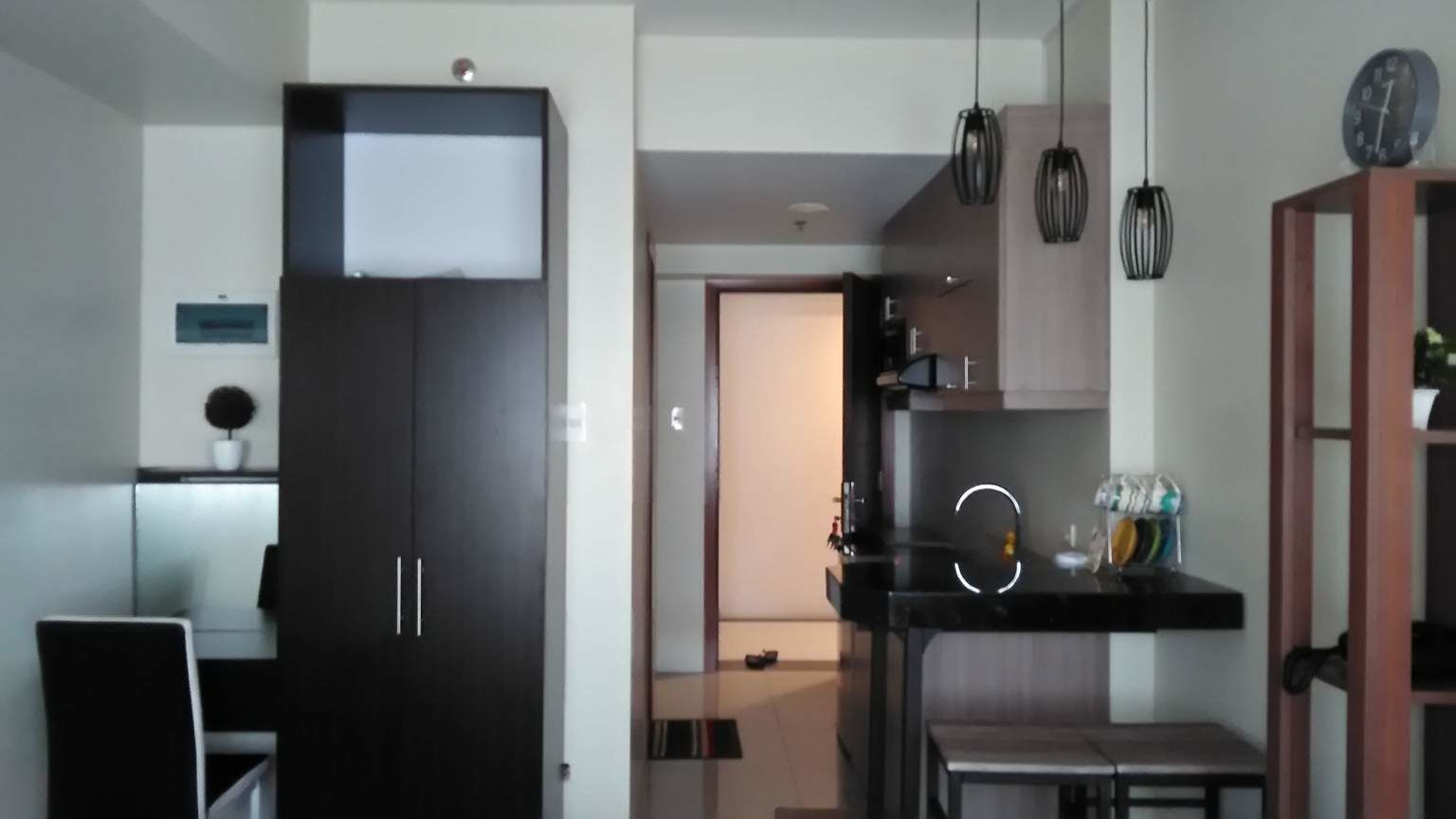 A modern kitchen with a black countertop, hanging pendant lights, and a clock on the wall.