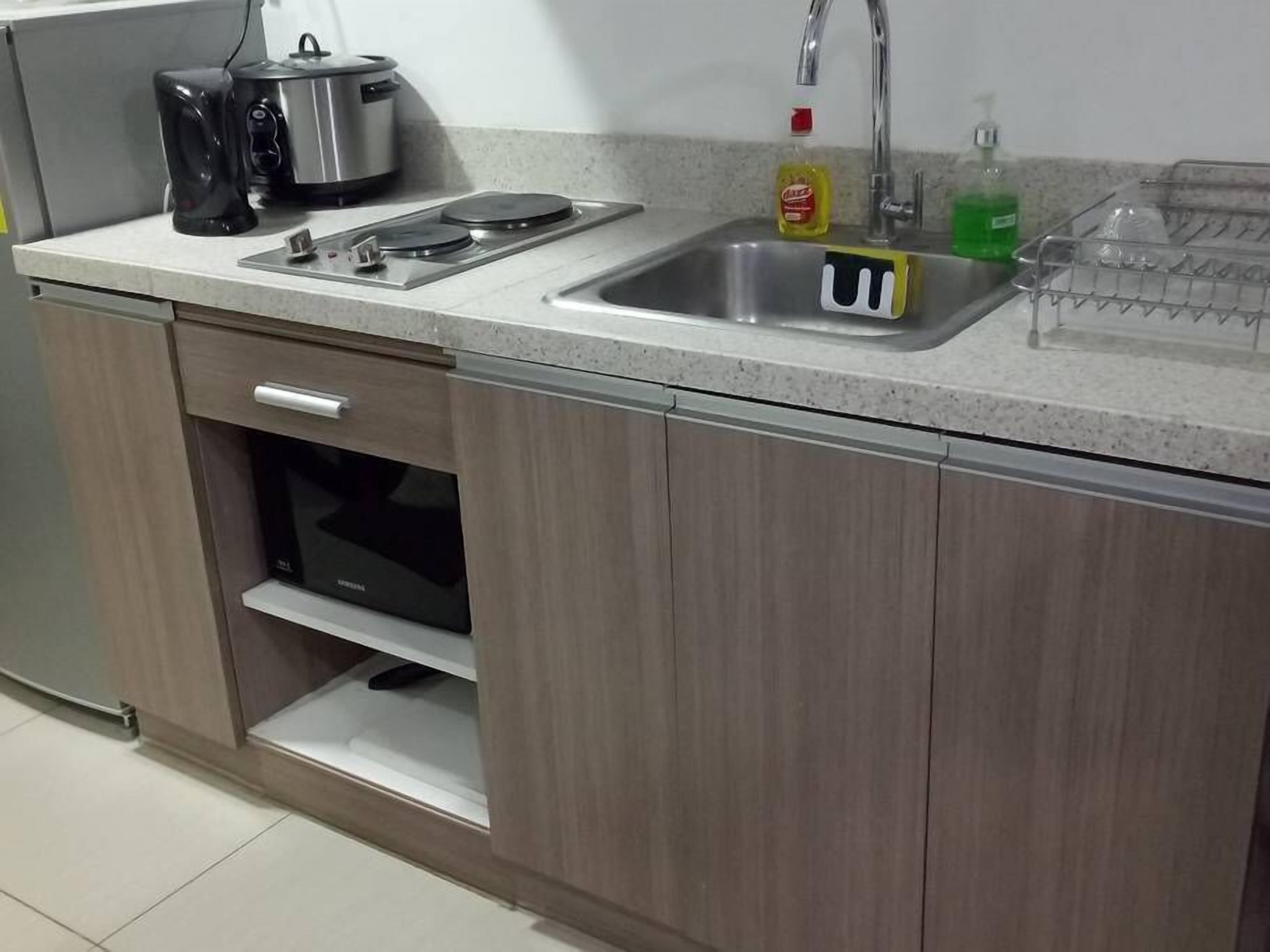 A kitchen with a stainless steel sink, a stove, and a microwave. There is a dish rack and a bottle of dish soap on the counter.