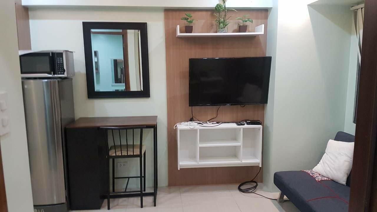 Un espacio habitable compacto con kitchenette, un televisor de pantalla plana montado en una pared de madera, una pequeña mesa y un sofá.