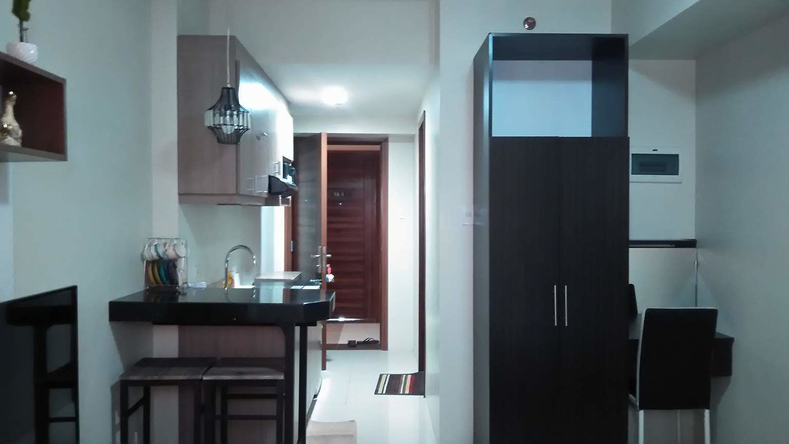 A compact kitchen with a black countertop, a hanging light fixture, and a dark wooden cabinet.