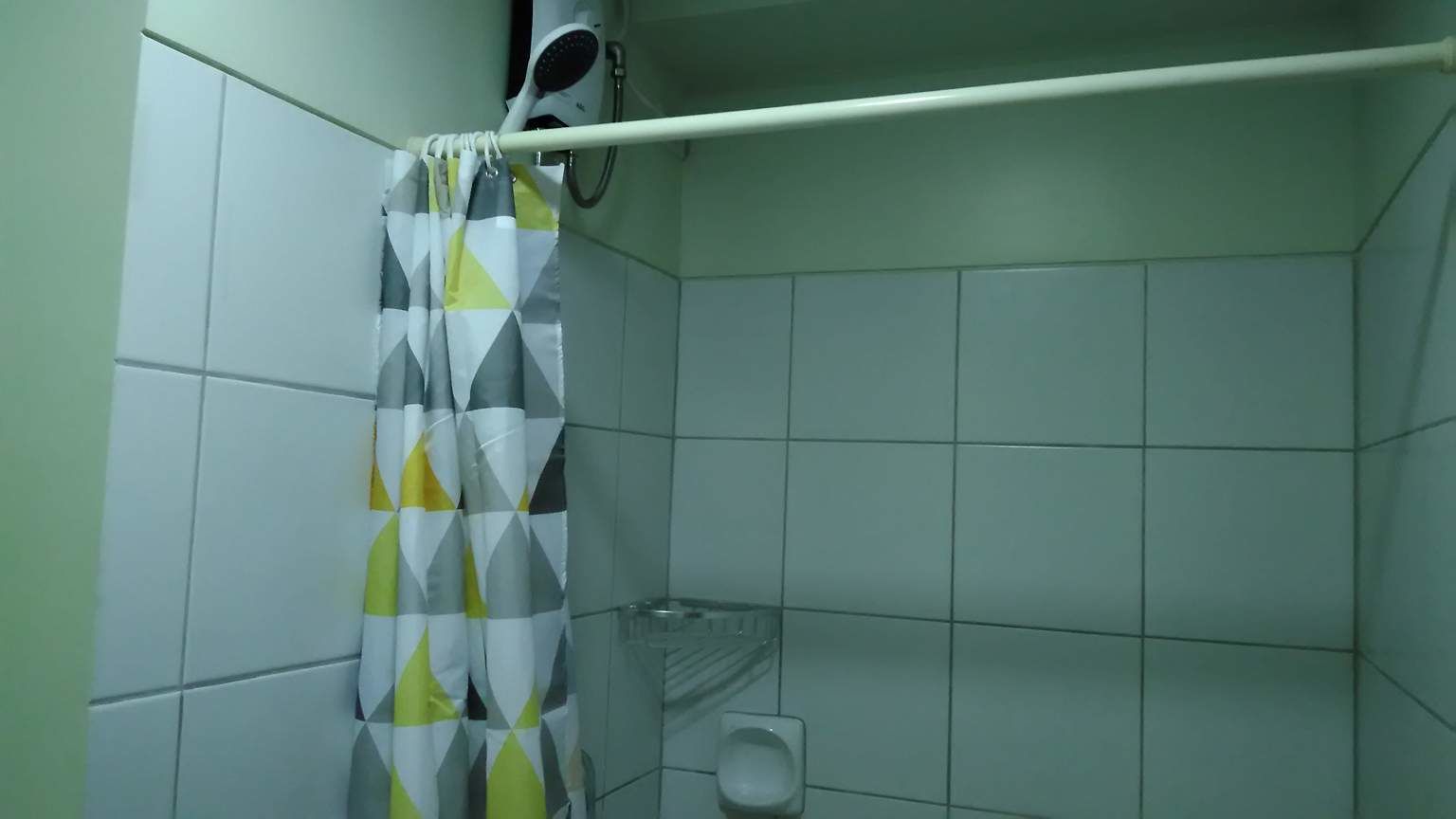 A bathroom with a shower curtain, a handheld showerhead, and a glass shelf.