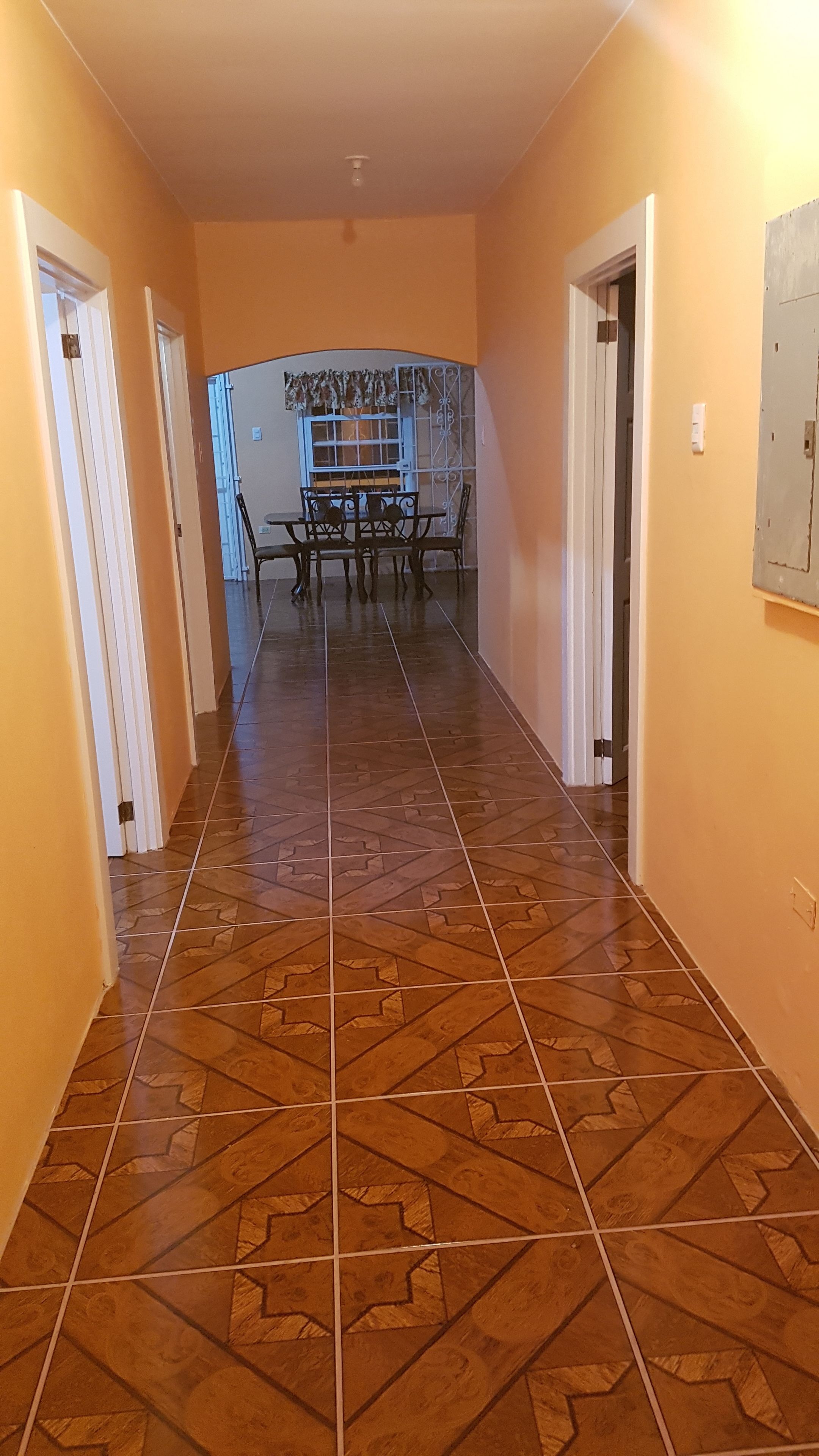 Un pasillo con suelo de baldosas estampadas, puertas blancas y, al fondo, un comedor con mesa y sillas.