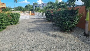 A gravel driveway leading to a house with a white fence and lush greenery. - Ri'Biero's Holiday Apartments (Crown Point)