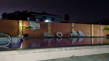 A nighttime pool area with lounge chairs, a pool with a tiled edge, and a wall with a 'No-eating or drinking in or around pool' sign.