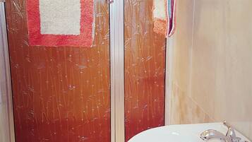 Un baño con lavamanos blanco, cabina de ducha de vidrio y toallero con toallas.