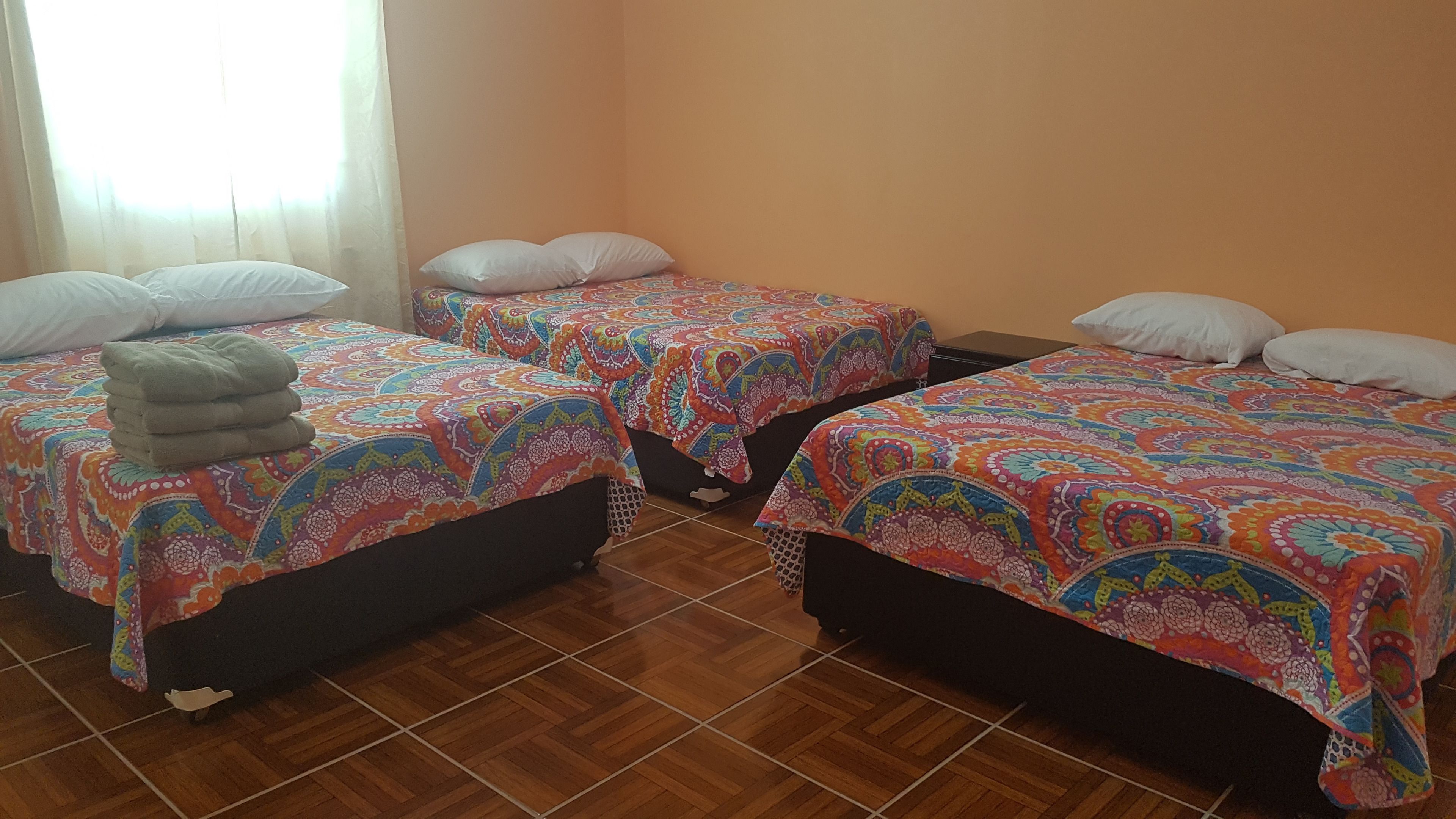 A room with three beds, each with colorful patterned bedding and white pillows.