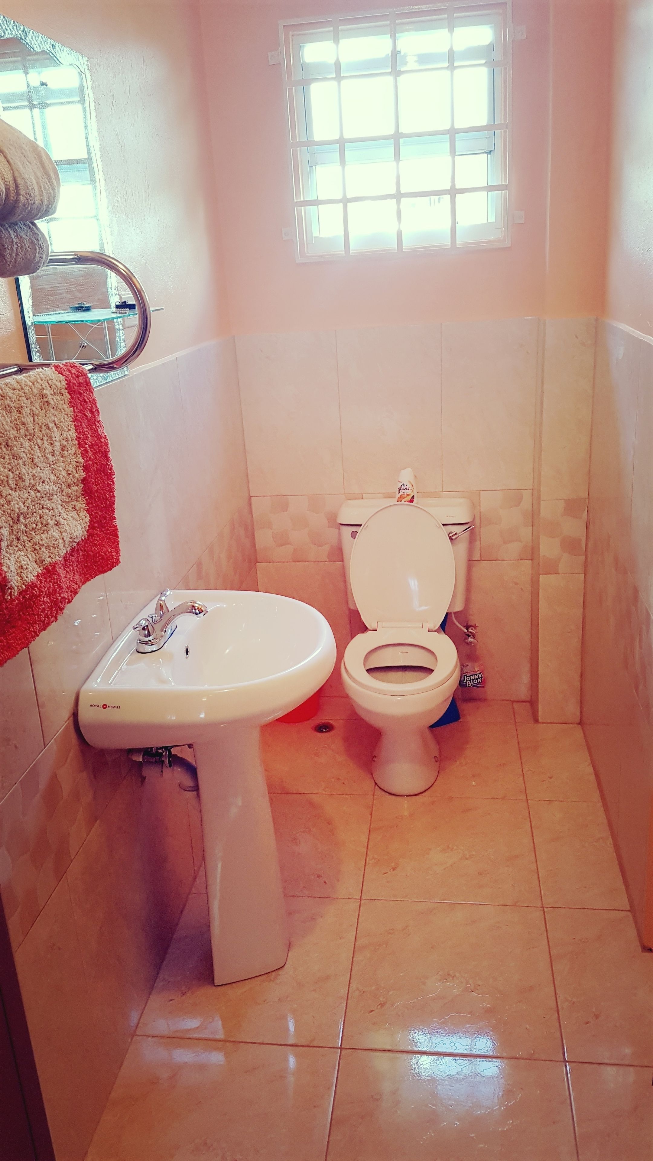 Um banheiro com vaso sanitário e pia, paredes revestidas de azulejos e uma janela com grades.