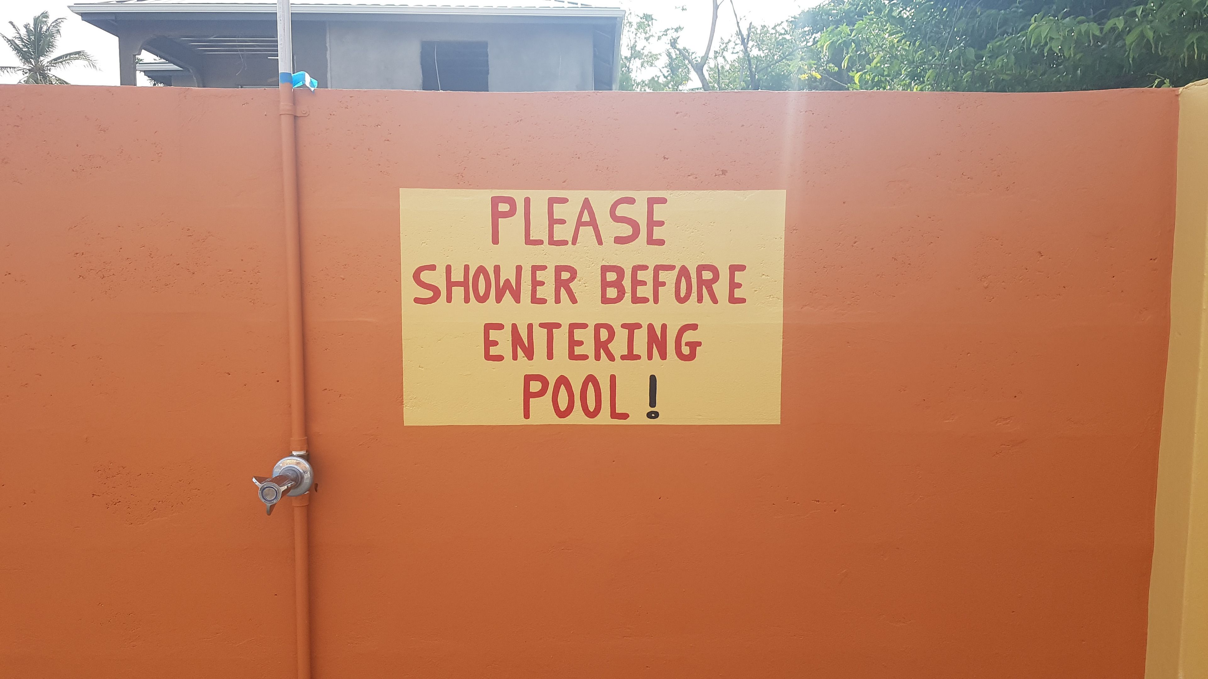 A sign on a wall that reads "PLEASE SHOWER BEFORE ENTERING POOL!"