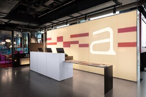 A modern reception area with a large illuminated 'a' sign, a reception desk, and a glass partition separating the reception from the lobby area. - Aloft by Marriott Dublin City (Dublin)
