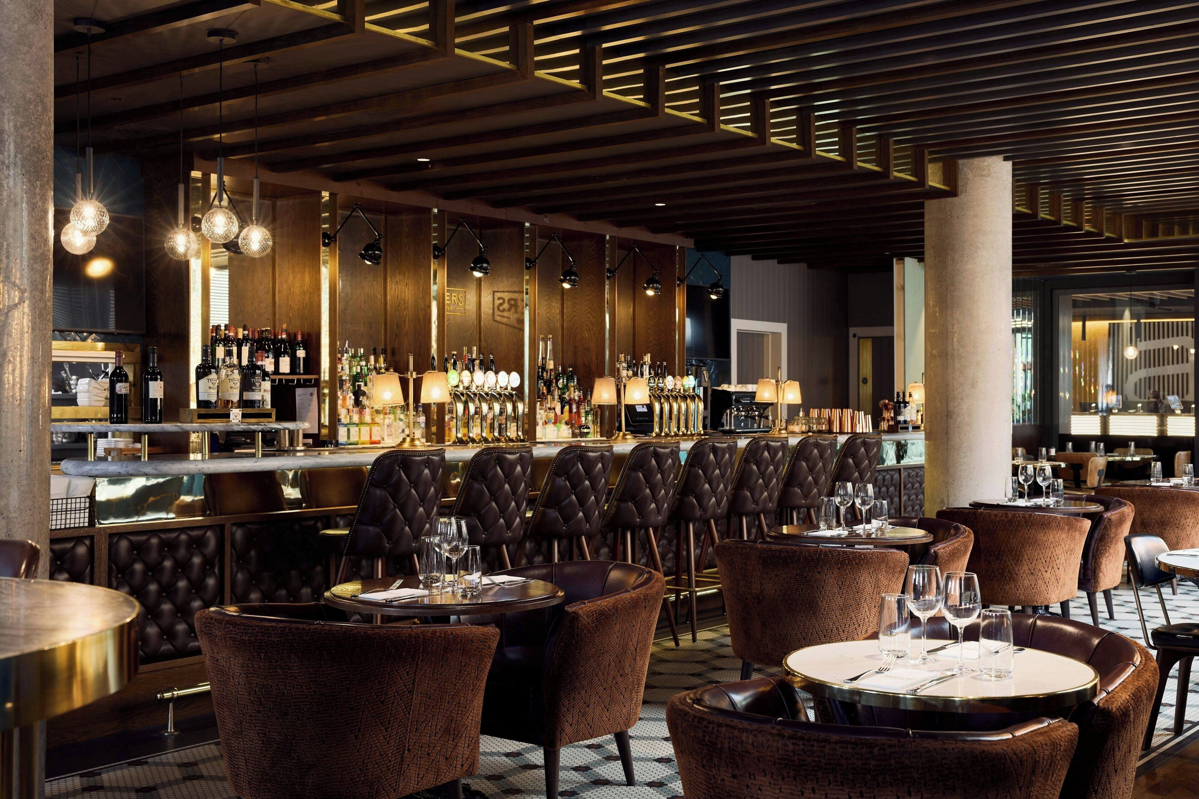 A bar area with multiple seating options, including round tables and cushioned chairs, and a well-stocked bar counter.