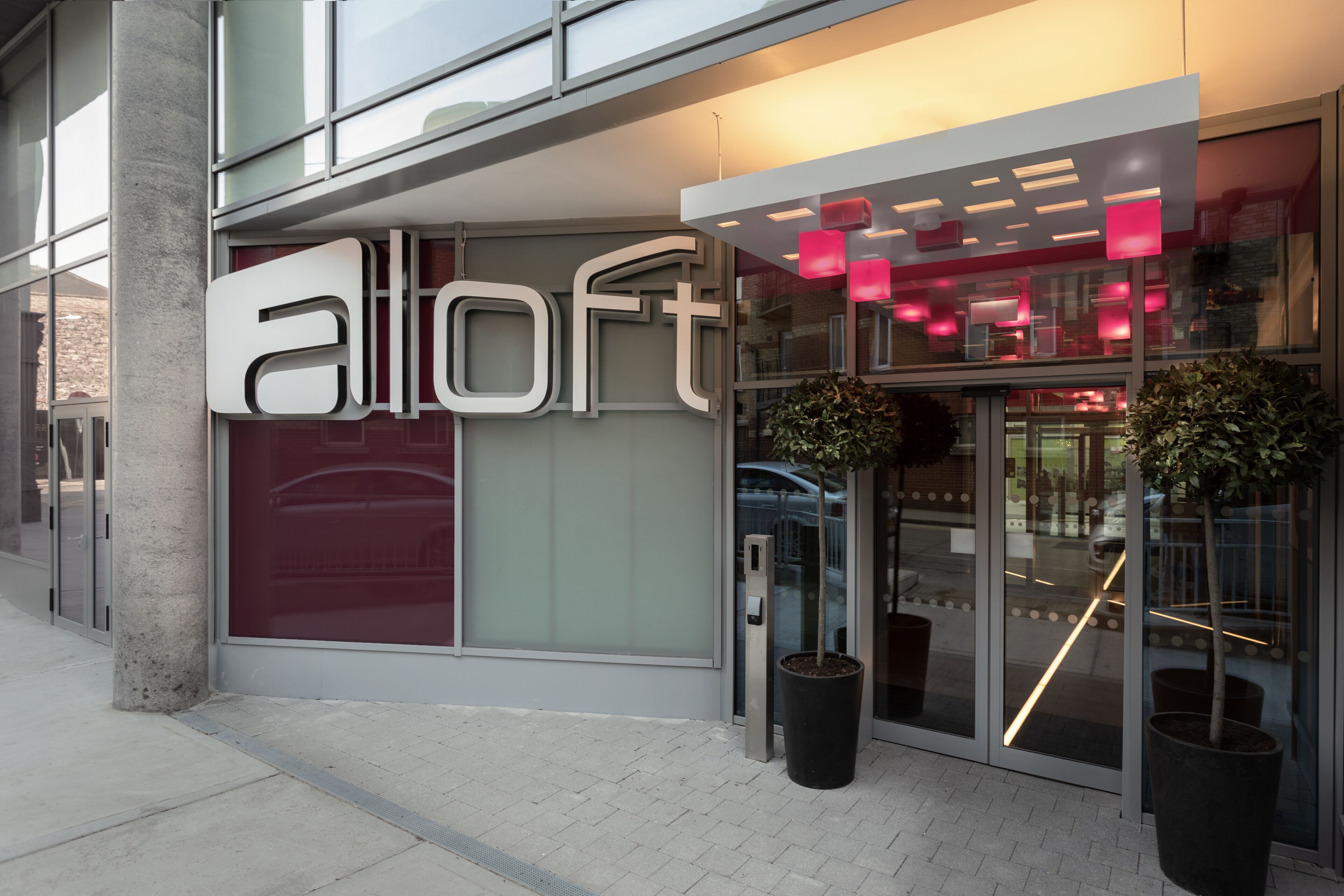 A modern building with a large glass entrance, a prominent 'Alloft' sign, and potted plants near the entrance.