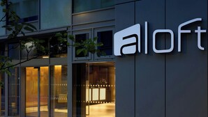 Un edificio moderno con fachada de vidrio y un llamativo letrero 'aloft'.