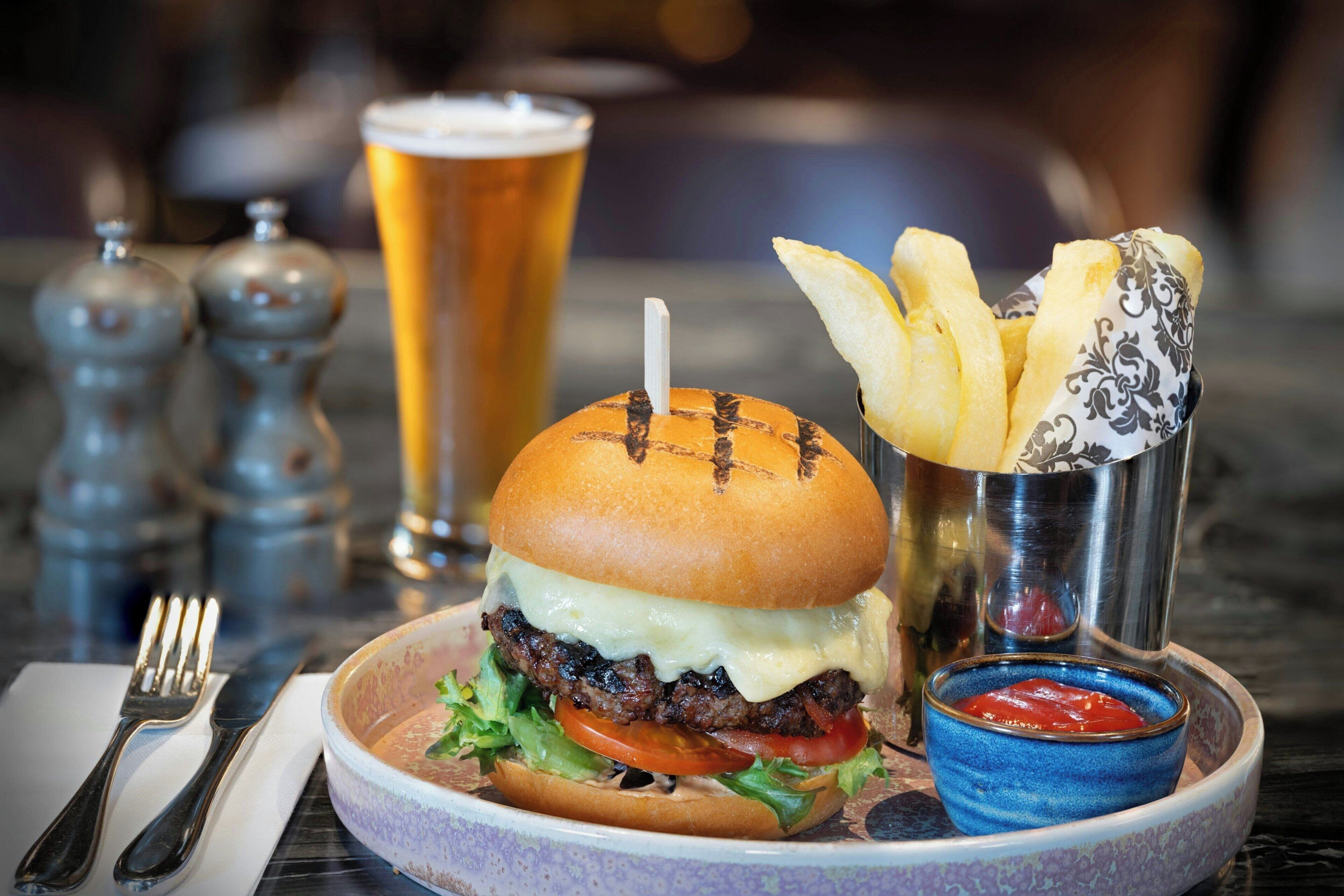 Una hamburguesa con papas fritas y una bebida sobre una mesa.