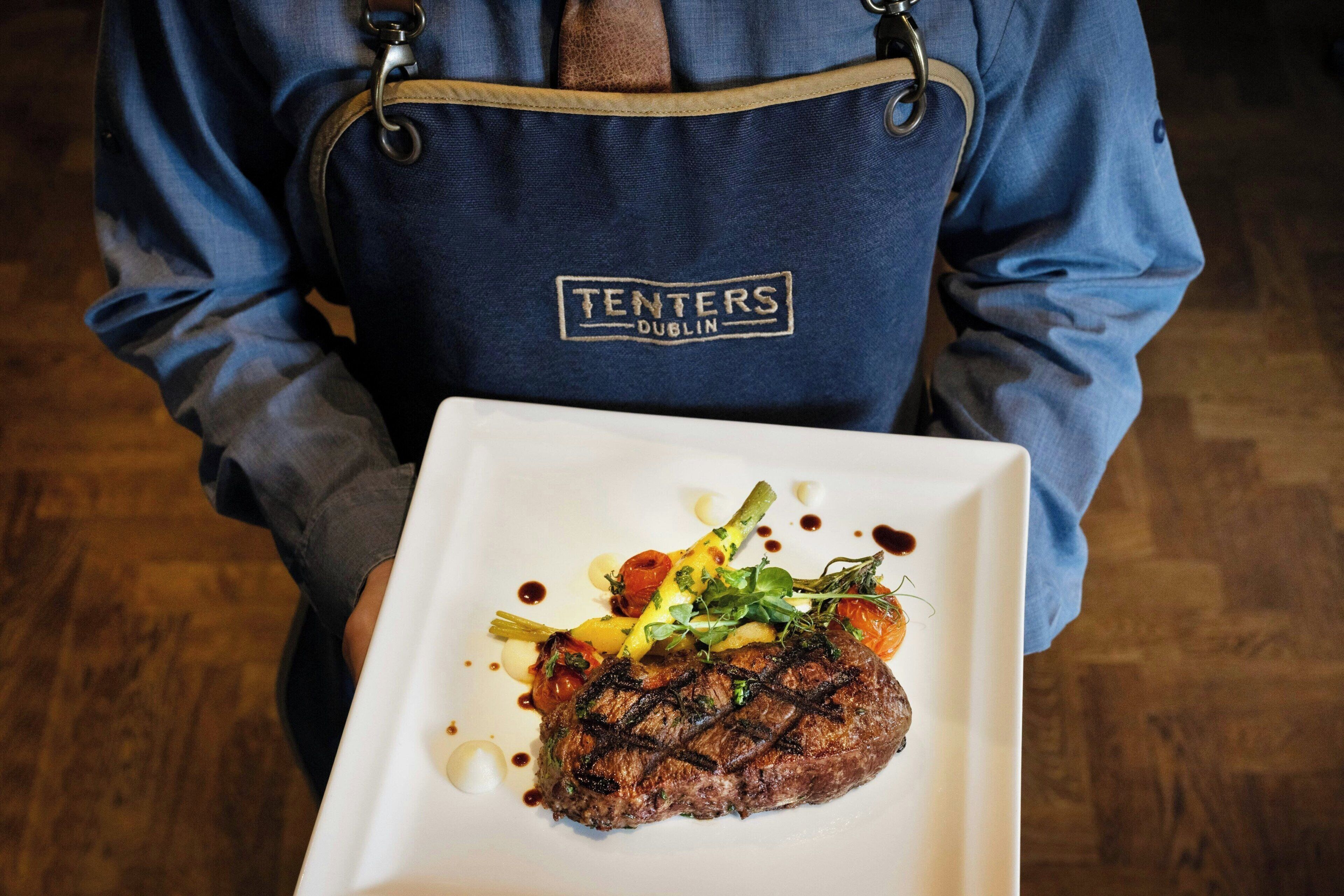 A person holding a plate with a steak and vegetables.