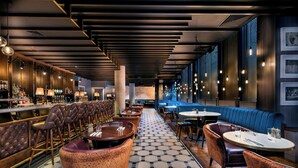 Zona de bar moderna con sillas de cuero, mesas redondas y suelo estampado.
