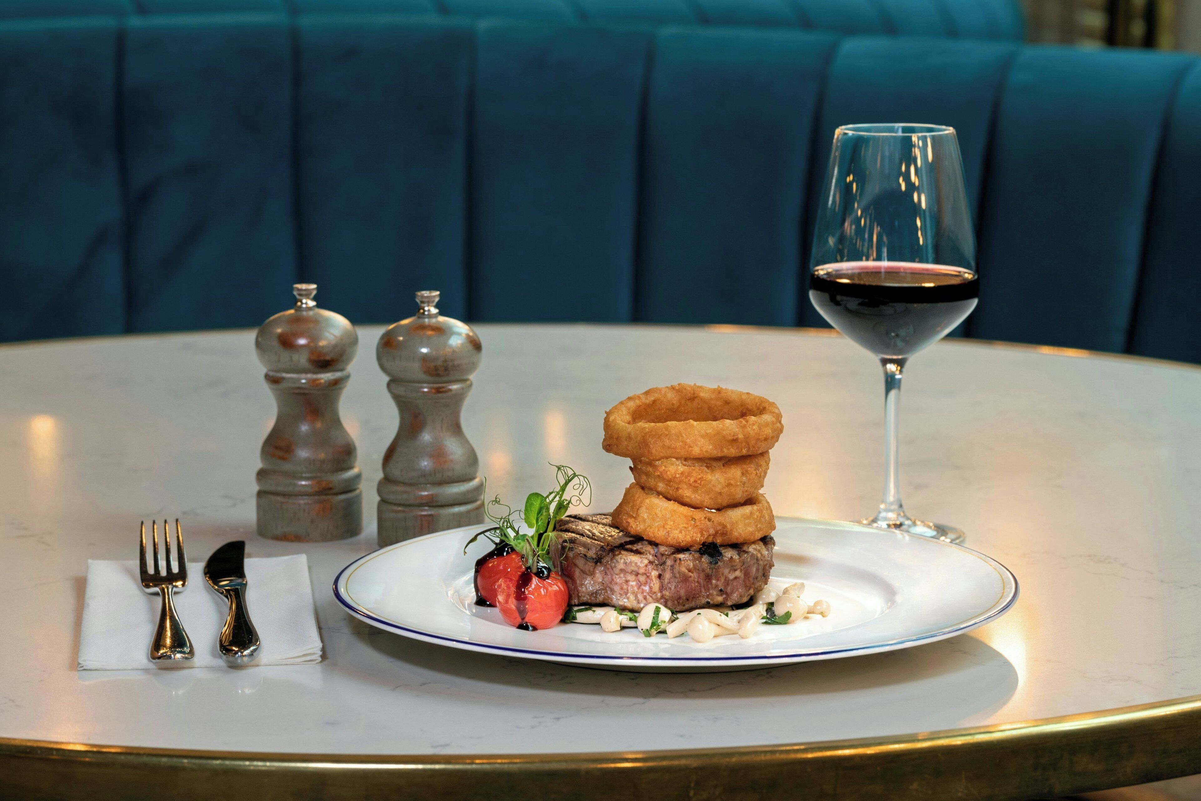 Una mesa de comedor con un bistec, aros de cebolla y una copa de vino tinto.