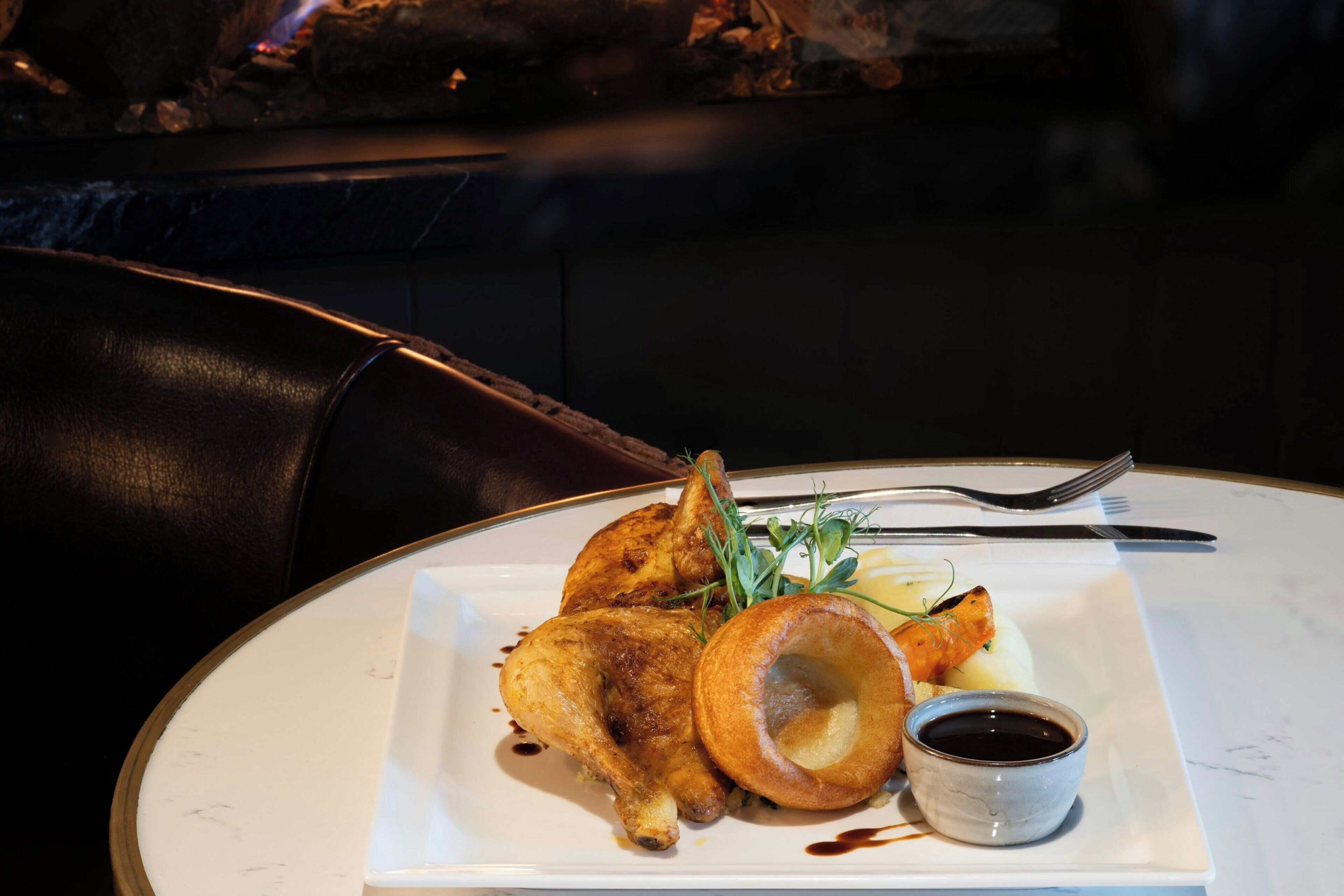 Een bord gebraden kip met Yorkshire pudding en jus, geserveerd op een wit bord met een klein schaaltje saus.