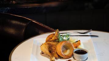 Een bord gebraden kip met Yorkshire pudding en jus, geserveerd op een wit bord met een klein schaaltje saus.