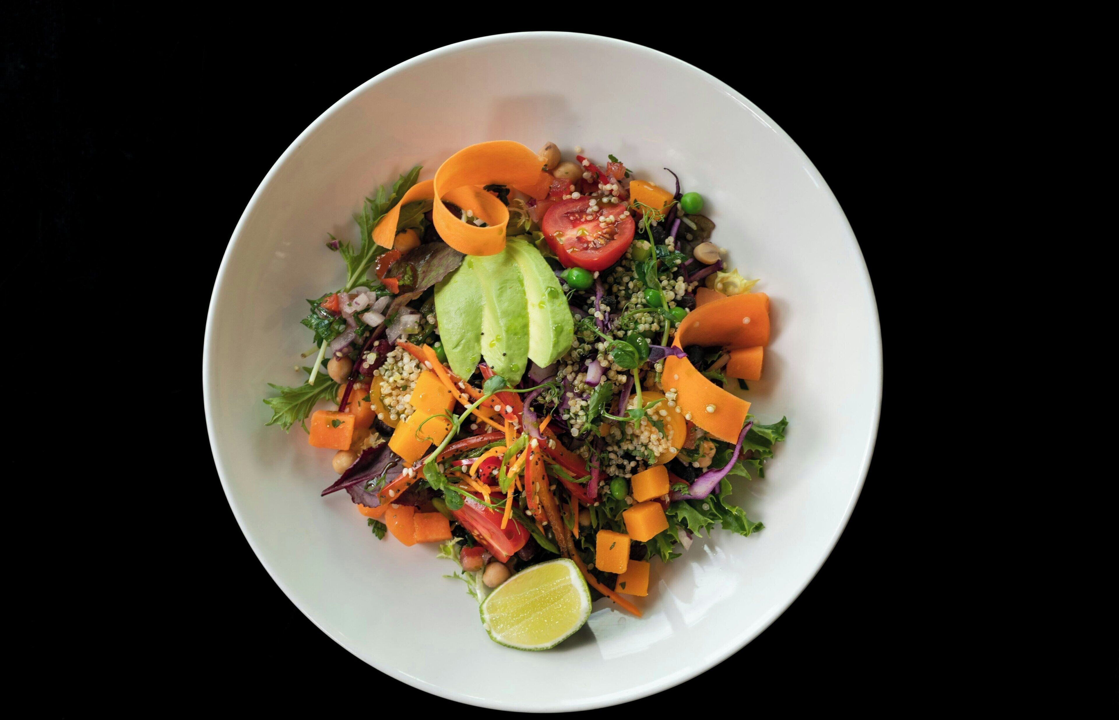 A bowl of salad with various vegetables and a lime wedge.