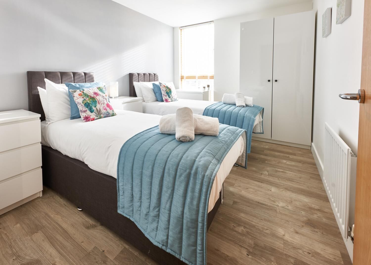 A modern bedroom with two beds, a wardrobe, and a radiator.