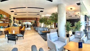 A modern hotel lobby with seating areas, a bar, and a variety of plants.