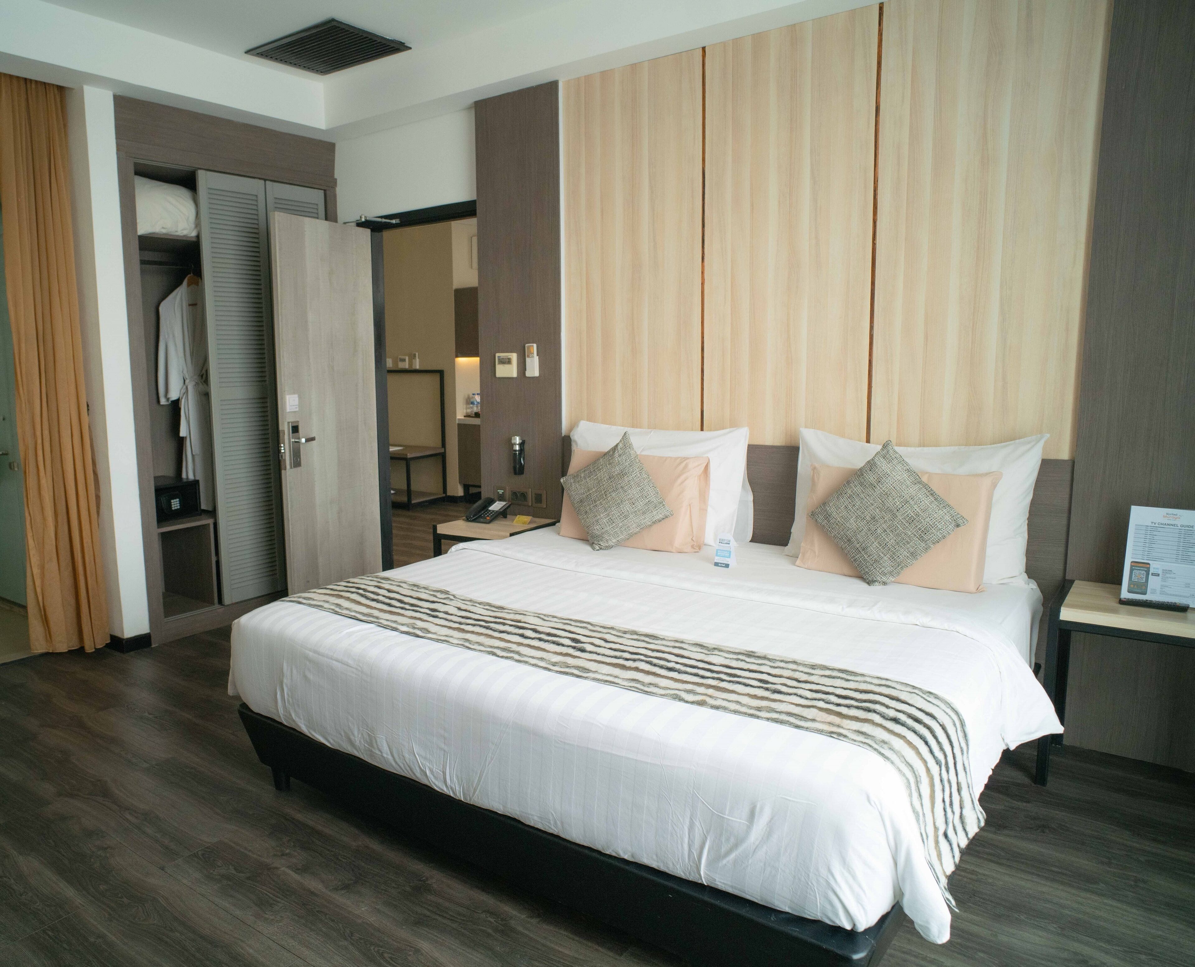 A hotel room with a large bed, a wardrobe, a bedside table with a lamp, and a mirror.