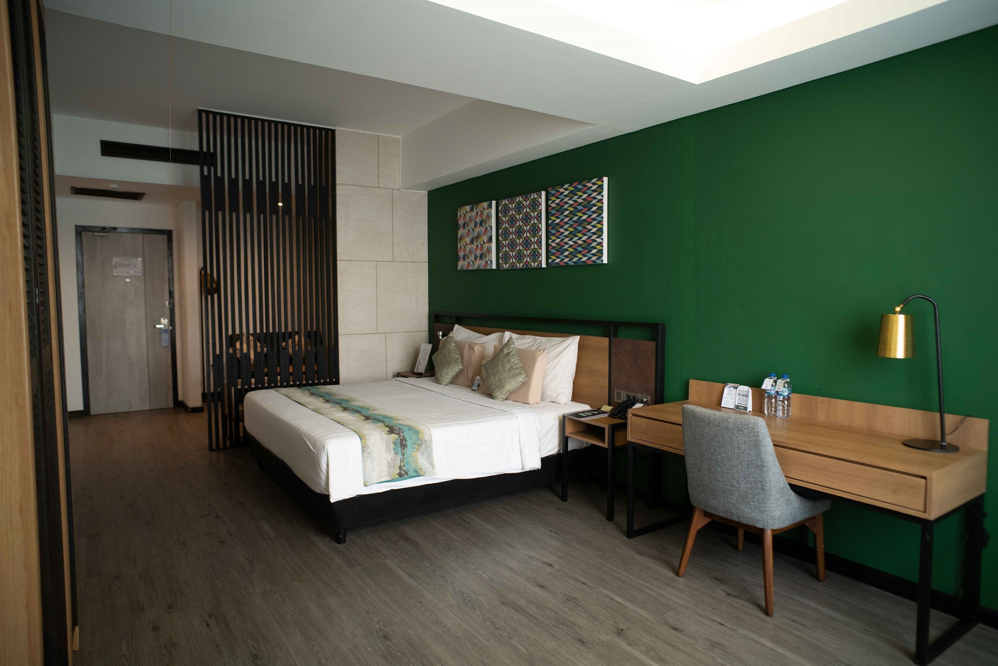 A modern hotel room with a bed, desk, chair, and green walls.