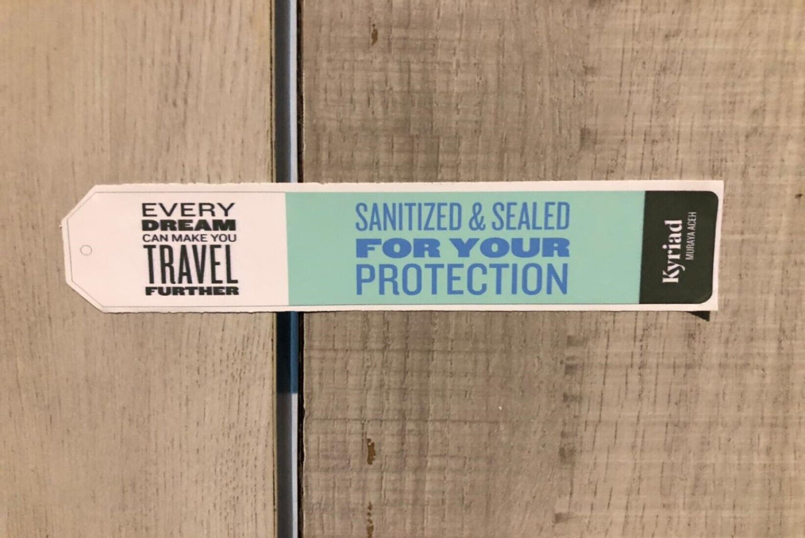 Ein Schild mit dem Text "EVERY DREAM CAN MAKE YOU TRAVEL FURTHER" und "SANITIZED & SEALED FOR YOUR PROTECTION" auf einer Holzfläche.