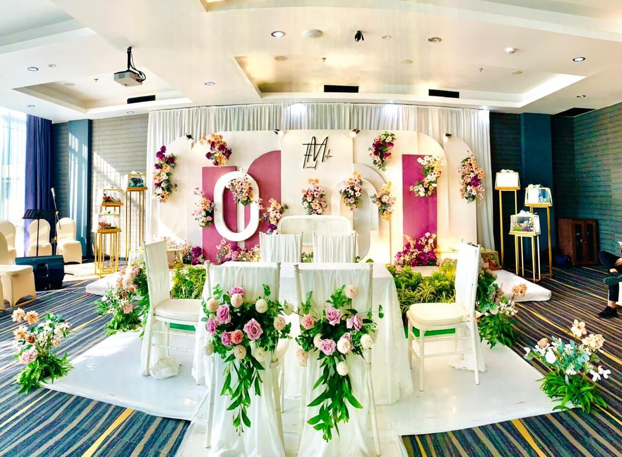 A wedding reception setup with a stage, floral arrangements, and white chairs.