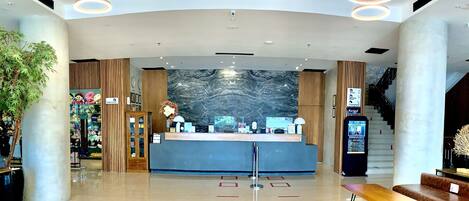 A modern lobby with a reception desk, a marble wall, and a staircase.