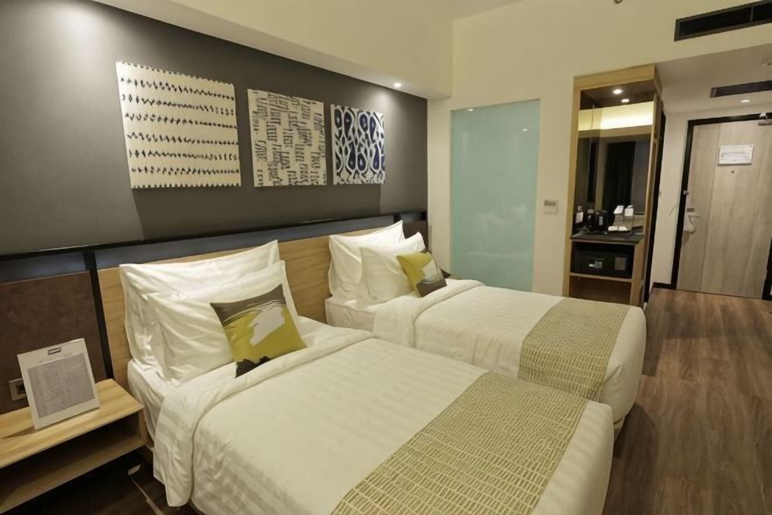 A hotel room with two beds, a wooden headboard, a mirror, a desk, and a wardrobe.